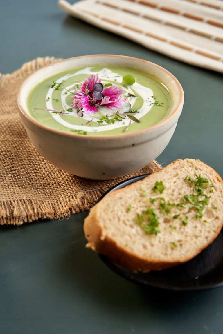 A delicious bowl of green soup garnished with edible flowers, paired with artisan bread on a rustic table setting.