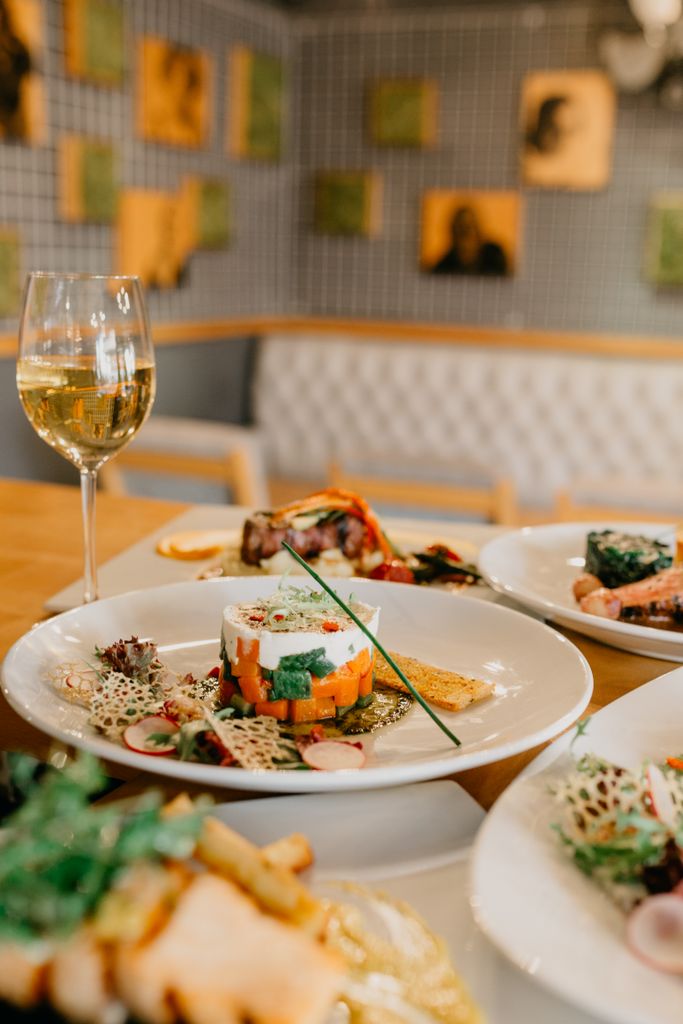 Served table with various delicious dishes and glass of white wine in modern restaurant on blurred background